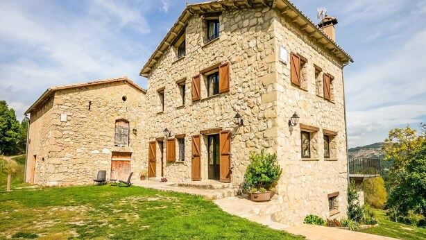 Ein Steinhaus mit einer großen Veranda, einem Schornstein und einem kleinen Garten mit einem Stuhl und Topfpflanzen.
