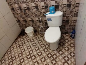 Baño con inodoro, un balde y manguera de ducha.