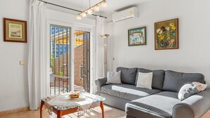 A living room with a grey sofa, a glass coffee table with fruits, a floor lamp, and a view of a building through a glass door. - Family-Friendly Apartment with Private Terrace, Shared Pool, A/C & Wi-Fi (Benalmádena)