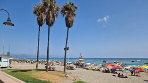 A beach with palm trees, umbrellas, and beach chairs. - Family-Friendly Apartment with Private Terrace, Shared Pool, A/C & Wi-Fi (Benalmádena)