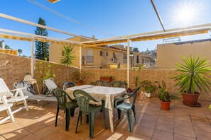 Une terrasse extérieure avec une table et des chaises, des plantes en pot et une vue sur les bâtiments en arrière-plan.