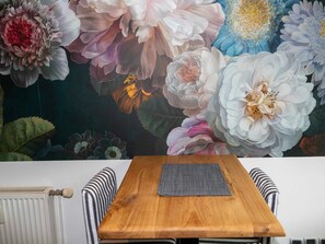A dining area with a wooden table and striped chairs, a radiator, and a floral mural on the wall.