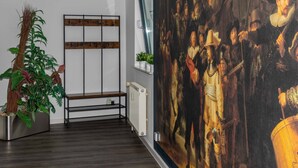 Una habitación con un cuadro clásico grande, un banco de madera, un radiador y una planta en maceta.
