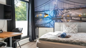 Una habitación de hotel moderna con una cama grande, un escritorio con una silla, un televisor de pantalla plana y un mural de un puente.