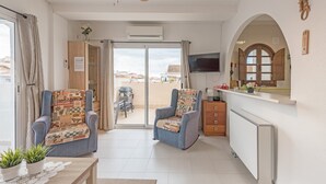 A modern living room with two armchairs, a coffee table with plants, a television, and a kitchen area with a window. - Penthouse Apartment Near the Beach with Sea View, Pool, Wi-Fi, A/C & Terrace (Torrevieja)