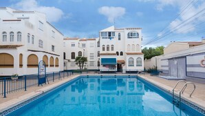 A swimming pool with a geometric tile border, surrounded by white buildings with arched windows and balconies, and a clear blue sky. - Penthouse Apartment Near the Beach with Sea View, Pool, Wi-Fi, A/C & Terrace (Torrevieja)