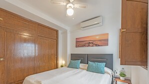 A bedroom with a large wooden wardrobe, a bed with a grey headboard, a small bedside table with a plant, and a wall-mounted air conditioner. - Penthouse Apartment Near the Beach with Sea View, Pool, Wi-Fi, A/C & Terrace (Torrevieja)