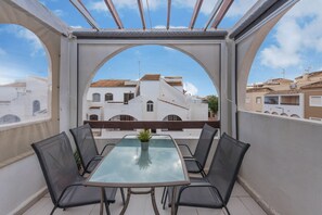 A balcony with a glass table and chairs, a potted plant, and a view of buildings.