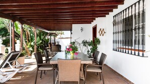 Un portico coperto con un tavolo da pranzo, sedie in vimini e piante in vaso.