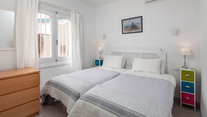 A bedroom with a bed, a dresser, a window with curtains, a bedside table with a lamp, and a wall-mounted picture. - Bright and Spacious Apartment near Beach with Shared Pool, A/C & Wi-Fi (Nerja)