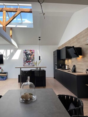 A modern kitchen with a skylight, a dining area with a glass-top table, and a kitchen island with a coffee machine. - Light-Filled Designer Apartment in Gütersloh - 90 m² - Flooded with Light (Gütersloh)