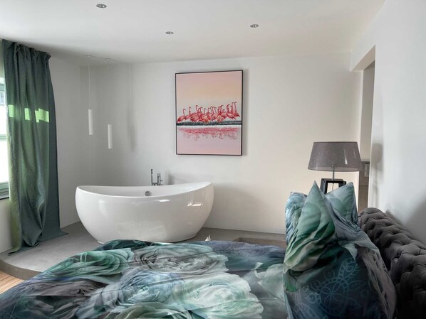A modern bathroom with a freestanding bathtub, a wall-mounted sink, and a large window with curtains. - Light-Filled Designer Apartment in Gütersloh - 90 m² - Flooded with Light (Gütersloh)