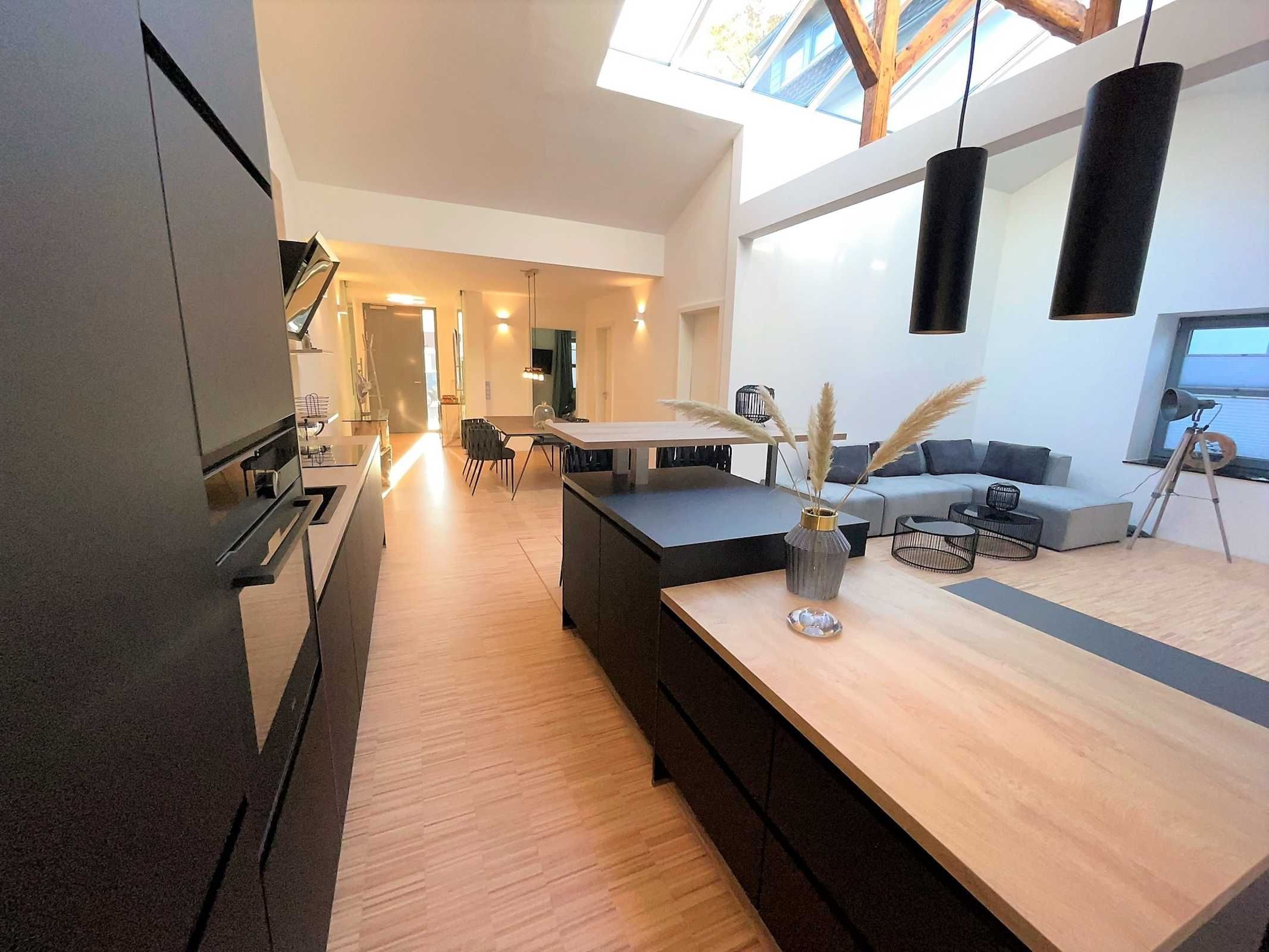 Una cocina moderna con una isla central, un comedor con mesa y sillas, y una sala de estar con sofá y un telescopio.