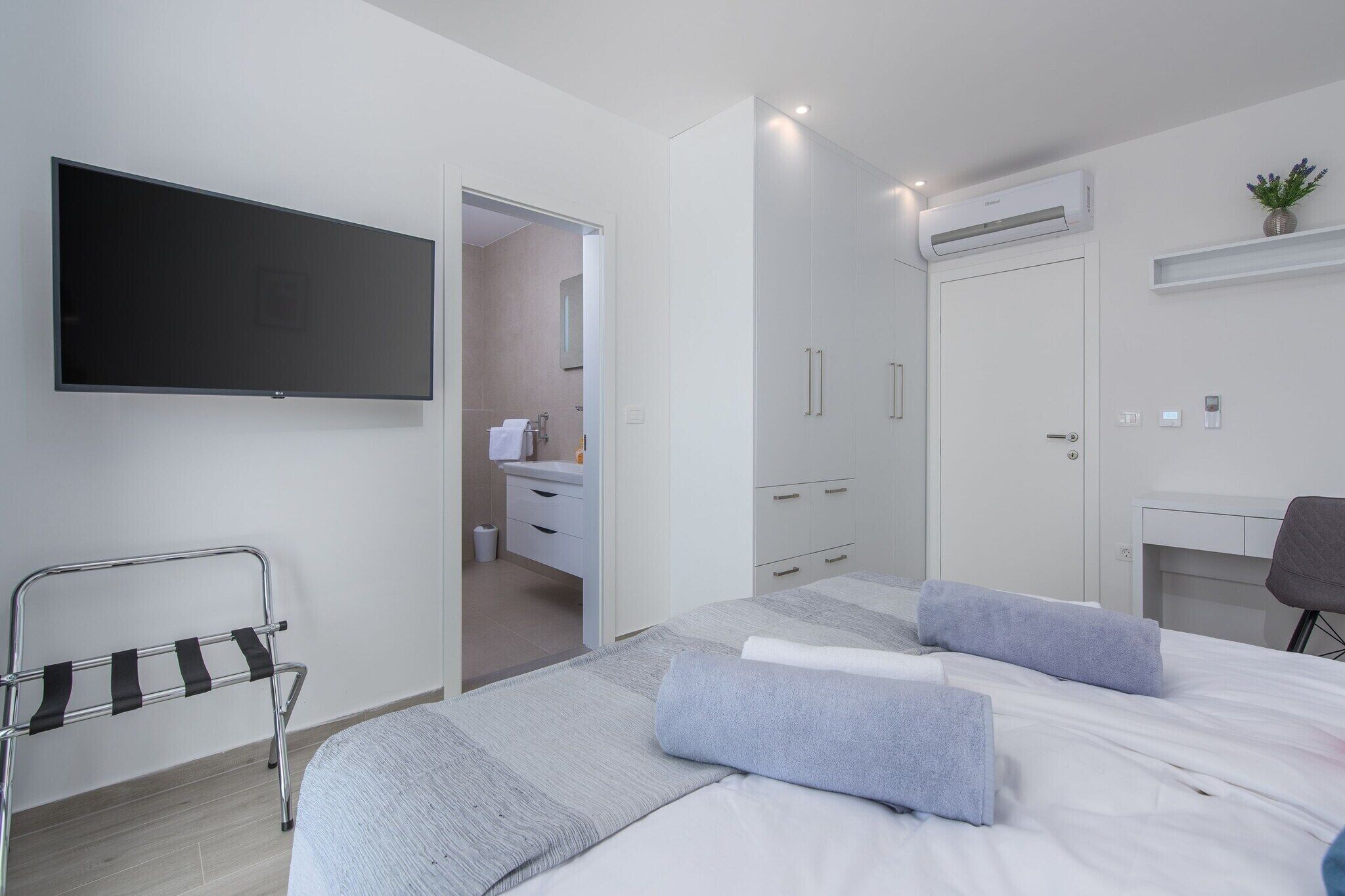 A modern hotel room with a bed, a TV, a desk, and a bathroom visible through an open door.