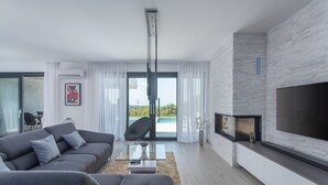 Un salon moderne avec un canapé gris, une table basse en verre, une cheminée et un grand téléviseur.
