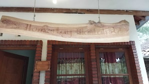 Un letrero de madera con la inscripción 'Homestay Hotel' colgado sobre una entrada de ladrillo con dos ventanas.