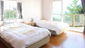 Un dormitorio con dos camas, una mesita de noche, una ventana con cortinas y un balcón con vistas a árboles y al mar.