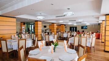 A spacious dining area with multiple round tables set for guests, featuring white tablecloths and neatly arranged place settings.