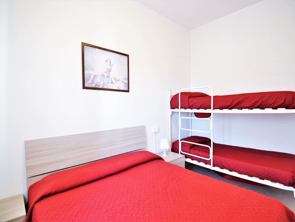 A bunk bed room with a wooden headboard, a framed picture on the wall, and a red blanket on the lower bunk.