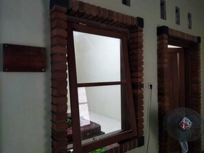 Una ventana con marco de ladrillo, un ventilador fijado a la pared y una puerta con arco de ladrillo.