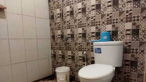 Ein Badezimmer mit Toilette, einem Eimer und gemusterten Fliesen an Wänden und Boden.
