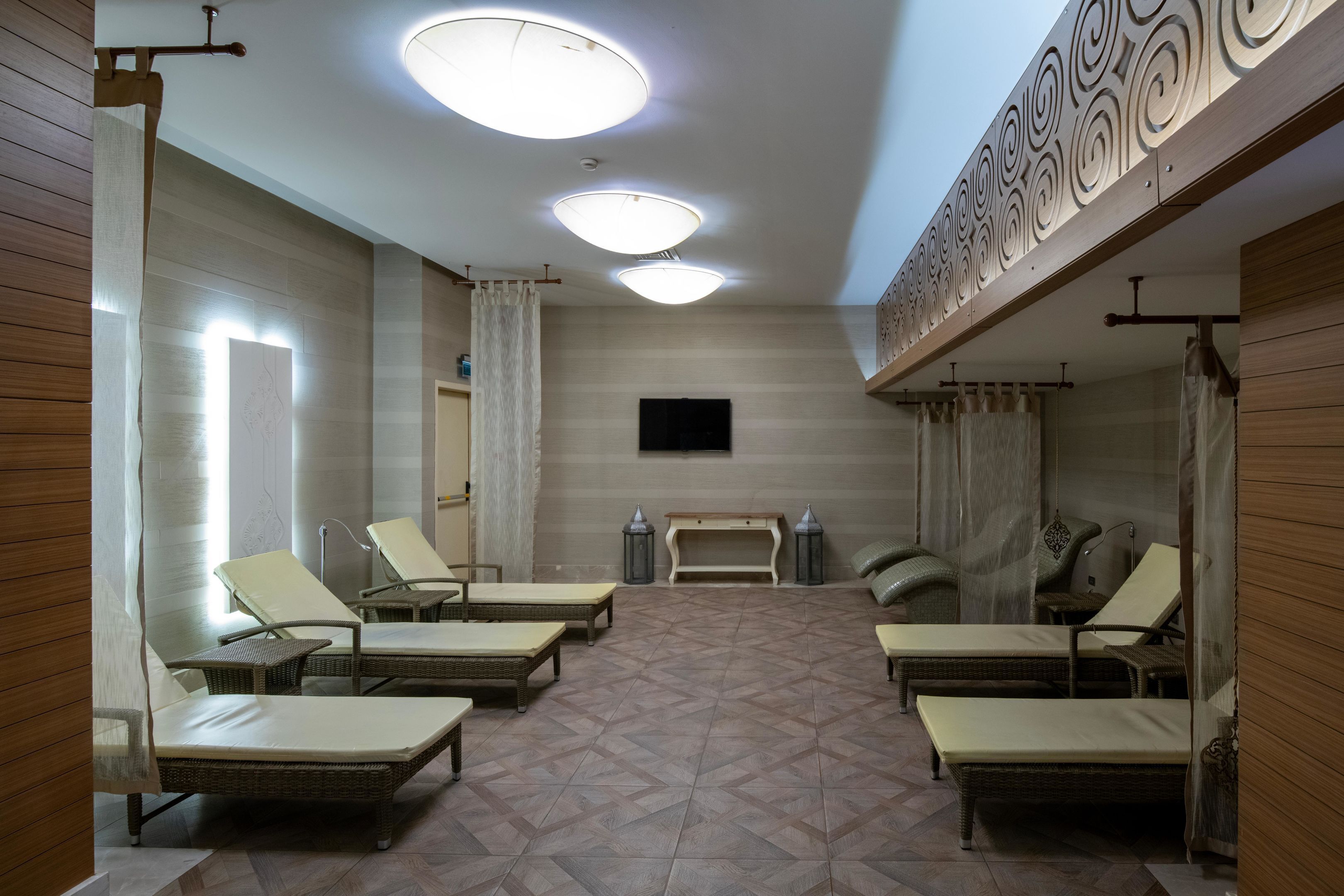 A room with four lounge chairs, a bench, a flat-screen TV, and a patterned floor.