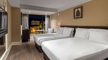 Habitación de hotel con dos camas, un escritorio, una silla, un televisor y vista a un paisaje urbano nocturno.