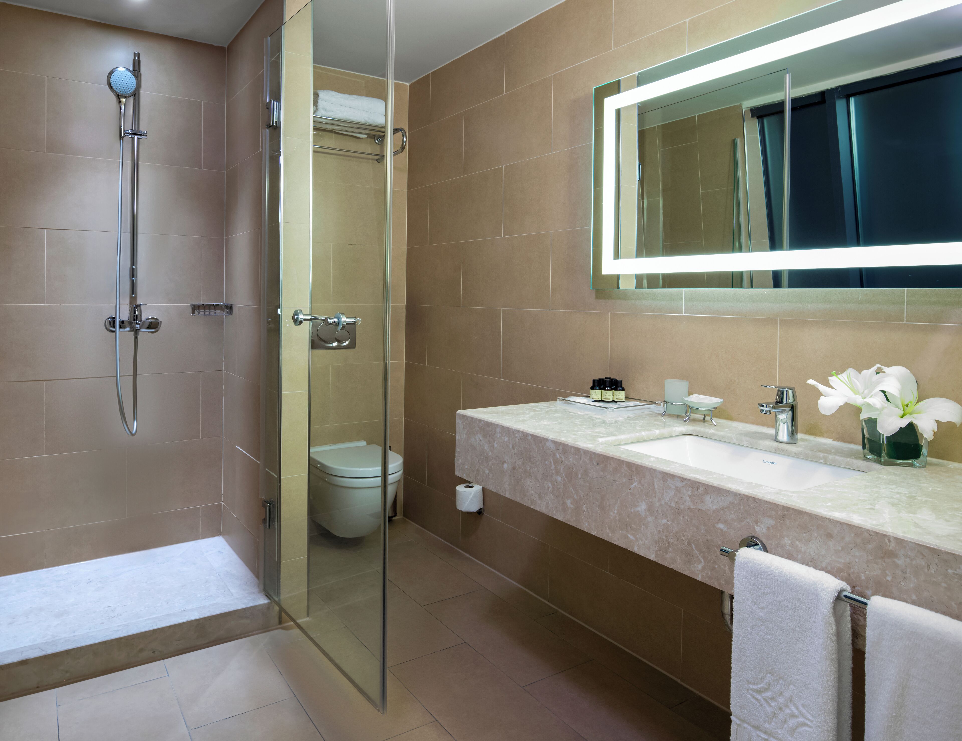 Un bagno moderno con doccia vetrata, un water, un lavandino con specchio e un porta asciugamani.