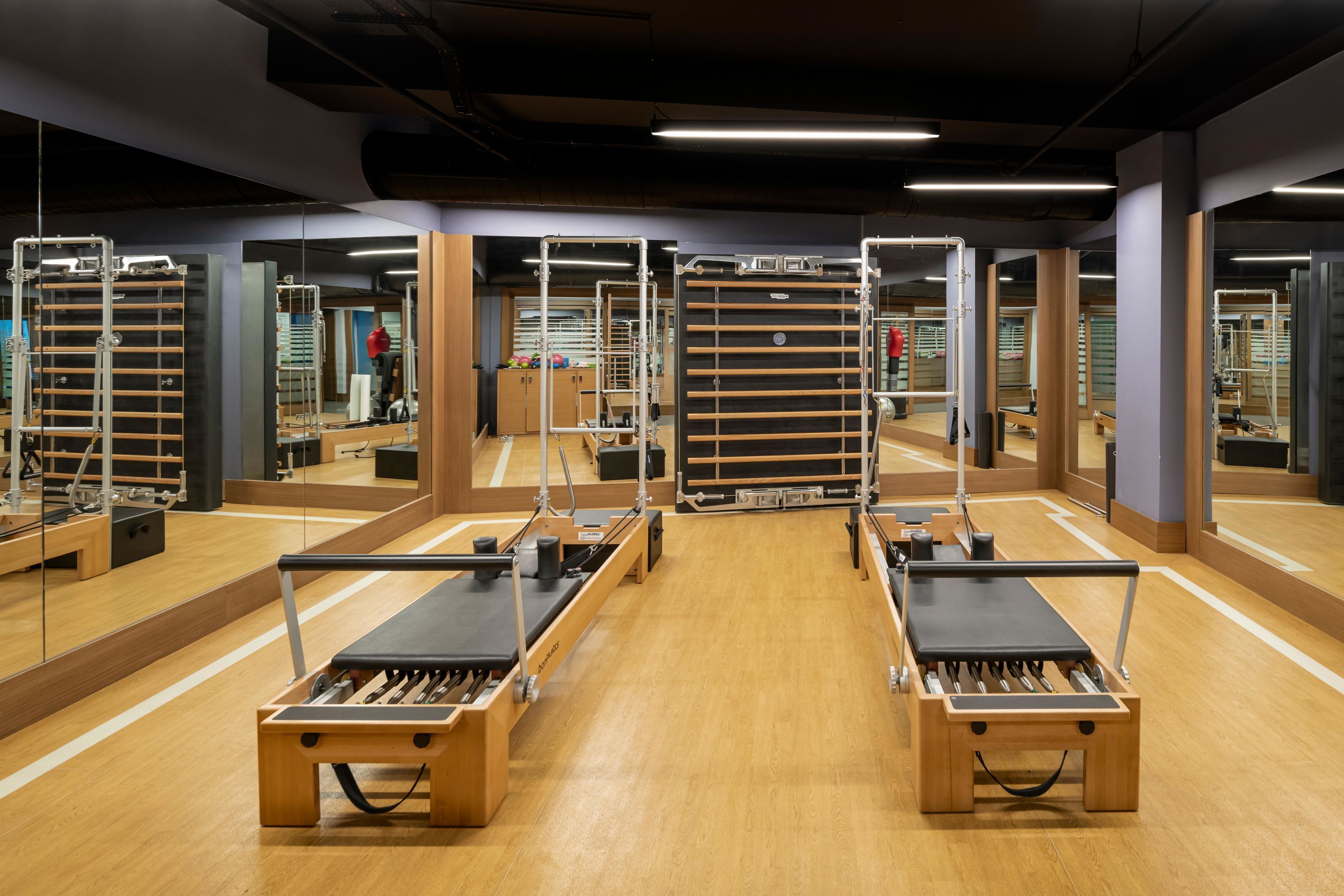 A Pilates studio with mirrored walls, wooden floors, and exercise equipment.