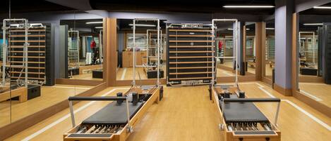 A Pilates studio with mirrored walls, wooden floors, and exercise equipment.