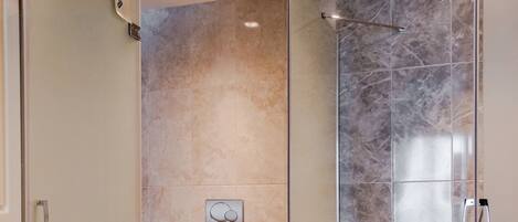 A modern bathroom with a glass-enclosed shower, a toilet, and marble tiles.
