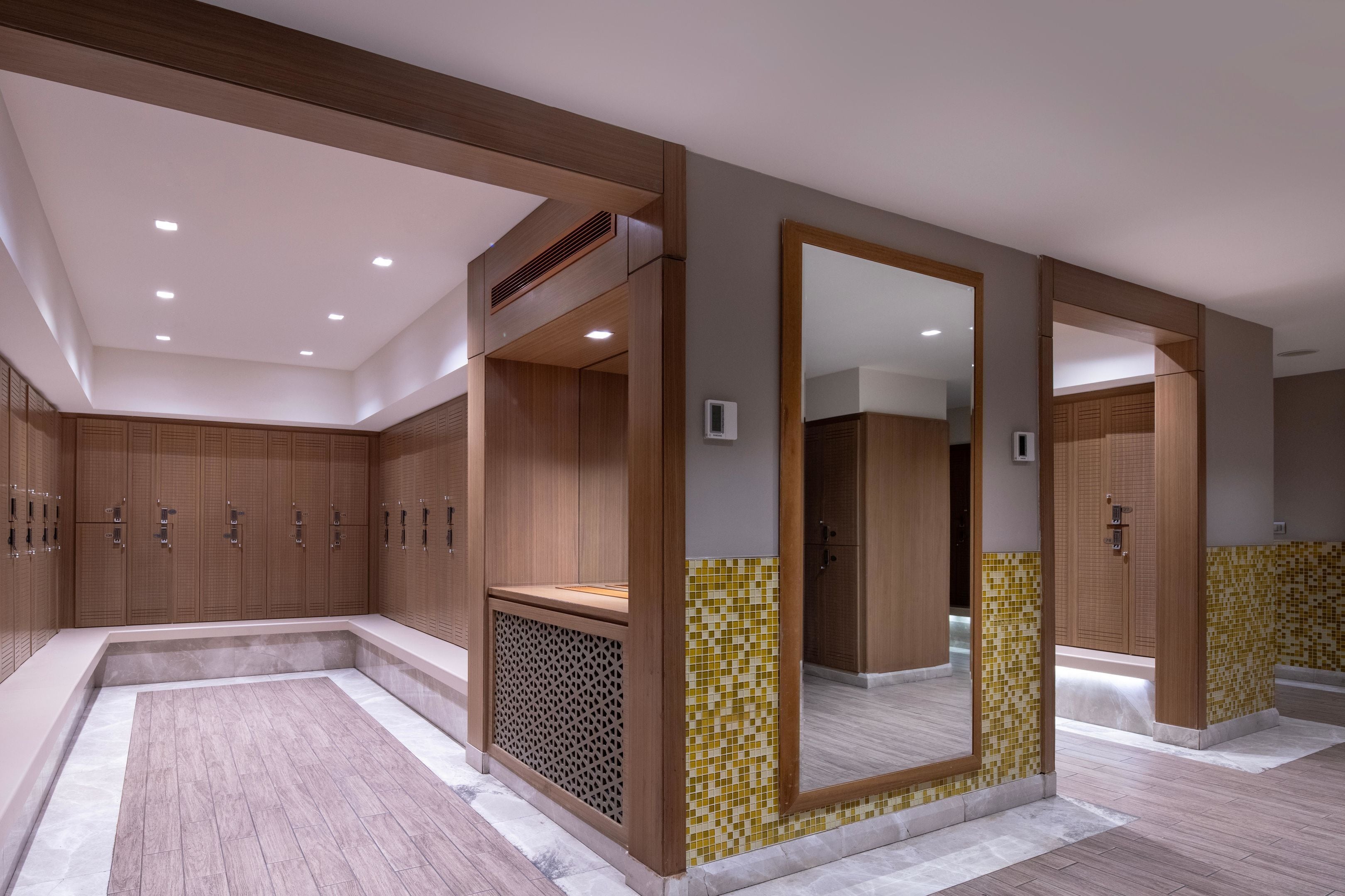 A modern bathroom with wooden lockers, a large mirror, and a tiled floor.