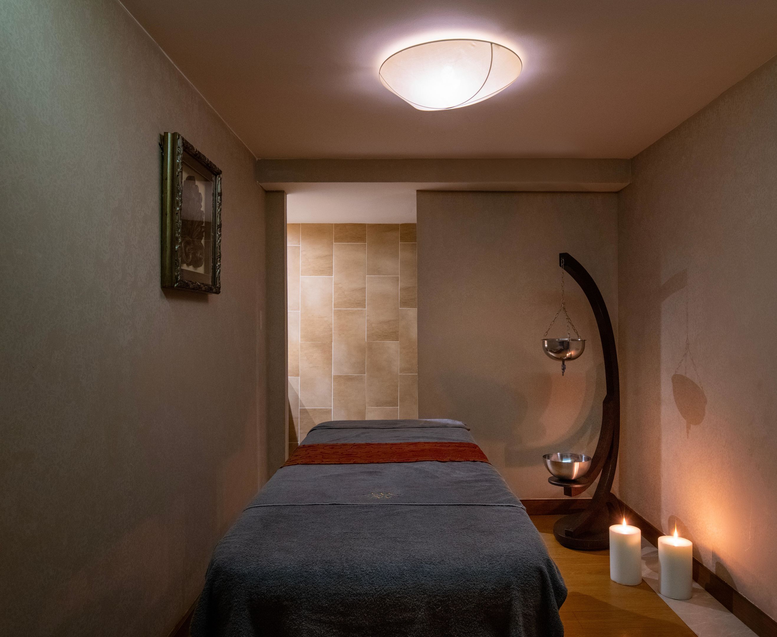 A spa room with a massage table, candles, and a wall-mounted bowl.