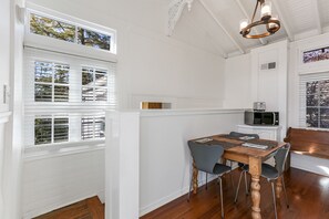 Un coin repas avec une table et des chaises en bois, un four à micro-ondes posé sur un meuble blanc, et une vue par la fenêtre.