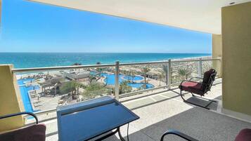 Un balcon avec une table et des chaises, donnant sur une piscine et une plage.