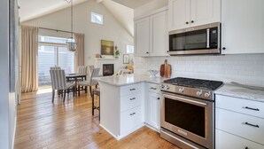 A modern kitchen with white cabinets, a built-in microwave, a gas stove, and a large island with a sink. - Art Collector's Sophisticated NW Crossing Home (Bend)
