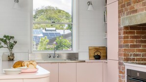 A kitchen with a window view of solar panels, a brick oven, and a small plant on the counter.