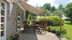 A patio with a table and chairs, a striped awning, and potted plants.