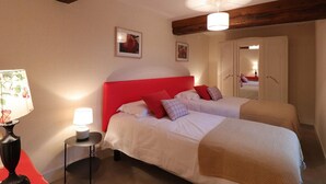 A hotel room with a red headboard, two beds, a small table with a lamp, and a mirror.