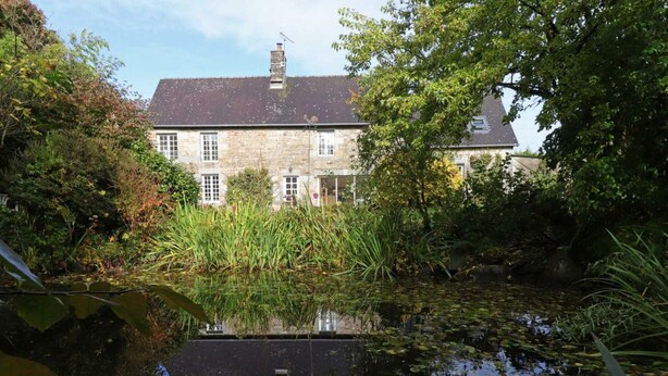 A stone building with a pond in front, surrounded by greenery.