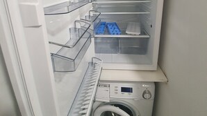 Ett kompakt kök med en inbyggd tvättmaskin, en mikrovågsugn och ett kylskåp med flera hyllor och fack.