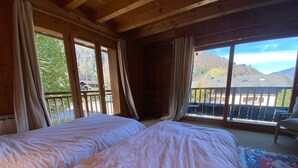 Una habitación con dos camas, ventanas amplias, un balcón y vistas a las montañas.