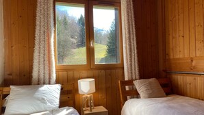 Una habitación tipo cabaña acogedora, con dos camas, una lámpara y una ventana con cortinas.