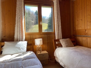 A cozy cabin room with two beds, a lamp, and a window with curtains.