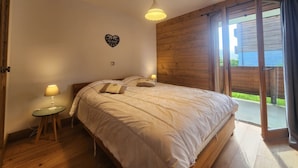 Une chambre à coucher comprenant un lit, des tables de chevet, un luminaire suspendu, un objet décoratif en forme de cœur et une porte-fenêtre coulissante donnant sur un espace extérieur.