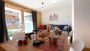 Un coin repas avec une table en bois, des chaises, un set de table rouge et une vue sur un balcon.