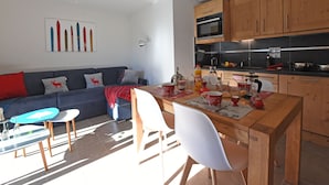 Un salon moderne comprenant un canapé, une table à manger avec des chaises, et un coin cuisine avec des meubles en bois et des appareils électroménagers.