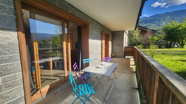 Une terrasse couverte avec une table et des chaises, une porte vitrée et une vue sur un paysage verdoyant.