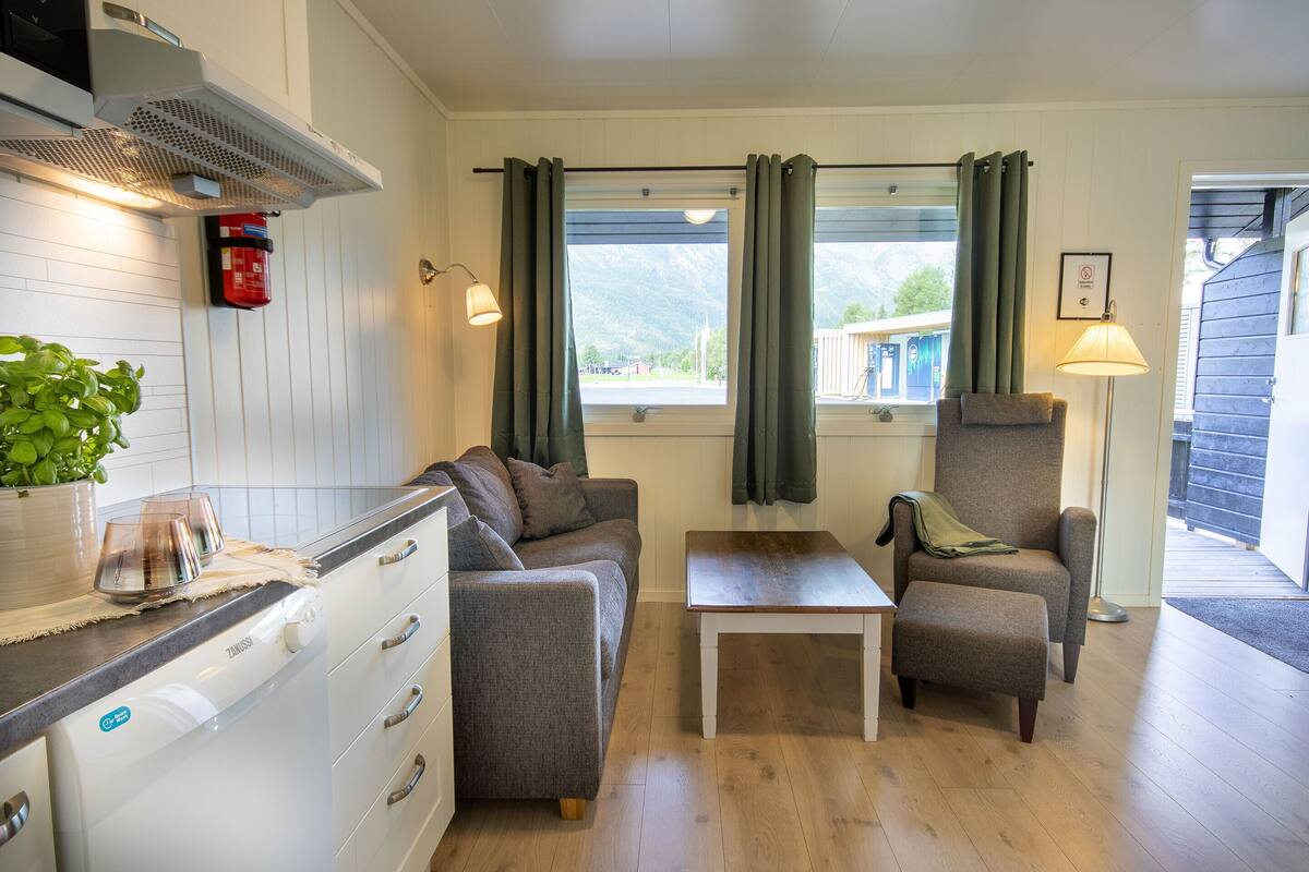 Un espacio habitable compacto con kitchenette, un sofá, una silla y una mesa pequeña.