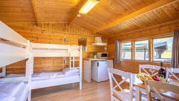 Una cabaña con literas, kitchenette, mesa de comedor con sillas y ventana con cortinas.